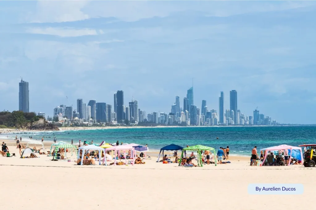 Beachgoers relaxing under colourful sun shelters on Burleigh Beach with the Surfers Paradise skyline visible in the distance, Gold Coast, Queensland.