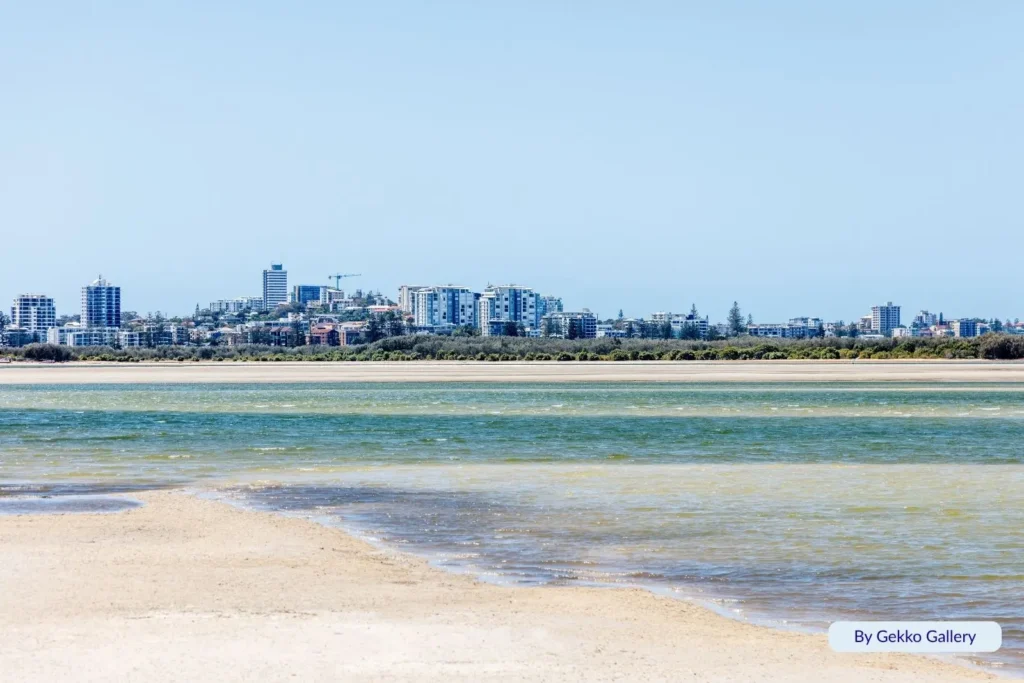 Sandy shore and calm tidal waters at Caloundra Beach with high-rise buildings in the distance under a clear blue sky, Sunshine Coast, Queensland