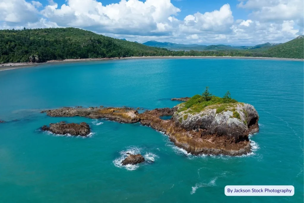 Turquoise waters and rocky outcrop off Cape Hillsborough National Park, Queensland, surrounded by lush coastal forest and blue skies