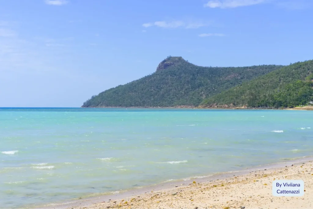 Peaceful shoreline and gentle waves with forested hills behind Catseye Beach on Hamilton Island, Whitsundays, Queensland.