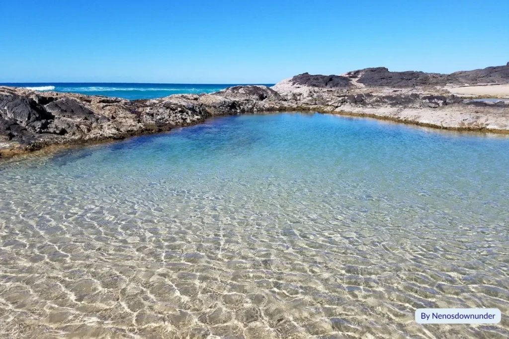 Clear shallow water inside the Champagne Pools on Fraser Island (K’gari), surrounded by dark volcanic rock and bright blue sky