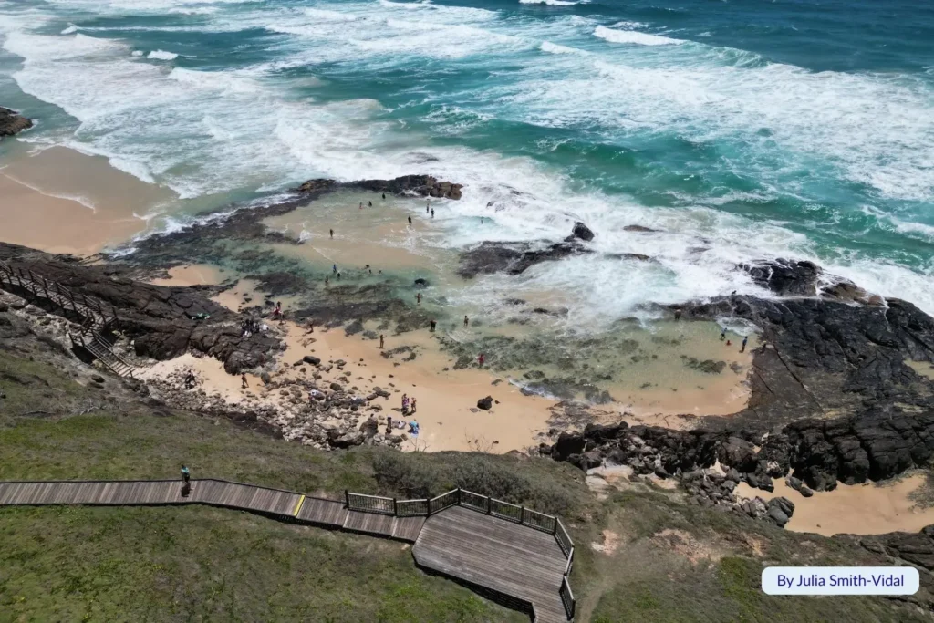 Champagne Pools on Fraser Island (K’gari), Queensland — visitors swimming in natural rock pools surrounded by golden sand, black volcanic rocks, and turquoise surf.