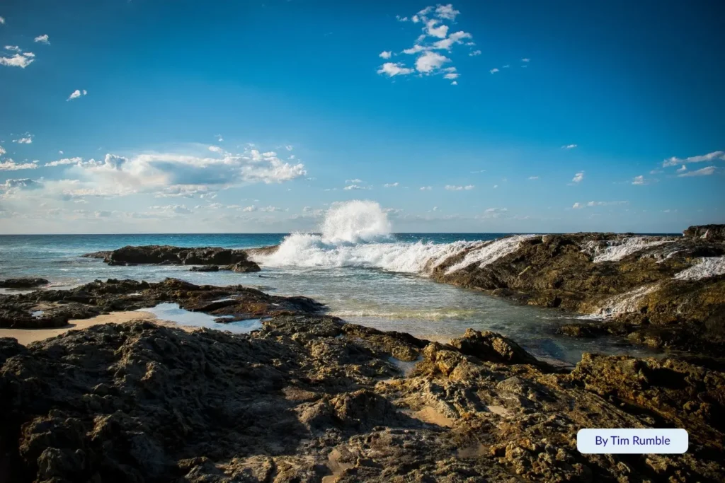 Waves crashing over natural rock pools at Champagne Pools on Moreton Island, Queensland, Australia, creating sparkling seawater bubbles under a bright blue sky