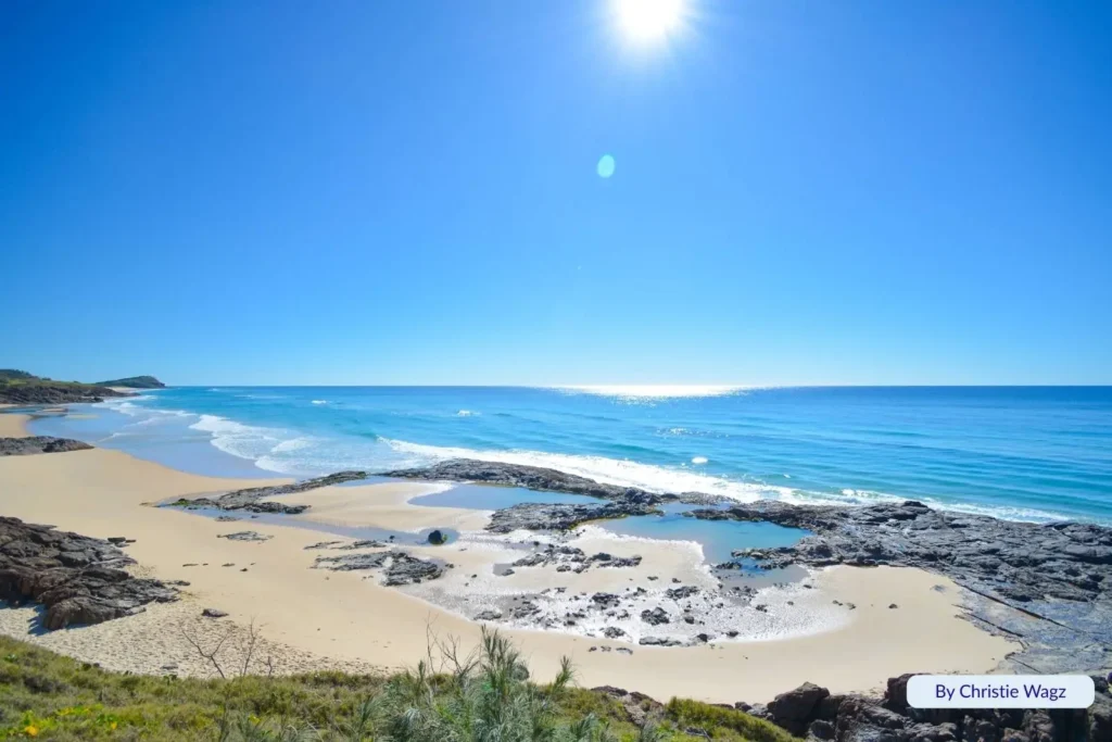 Champagne Pools on Fraser Island (K’gari), Queensland, with golden sand, volcanic rocks, and turquoise waves under a bright sunny sky.