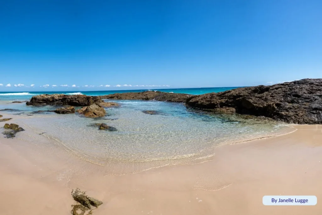 Champagne Pools on Moreton Island with clear rock pools, turquoise water, and volcanic rock formations under a bright blue Queensland sky.