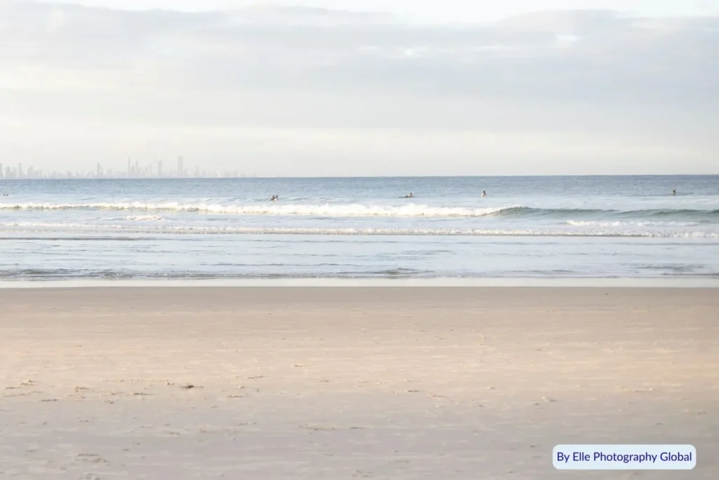 Surfers in the gentle waves at Cooee Bay Beach near Yeppoon, Queensland, with a golden sandy shore and coastal skyline in the distance