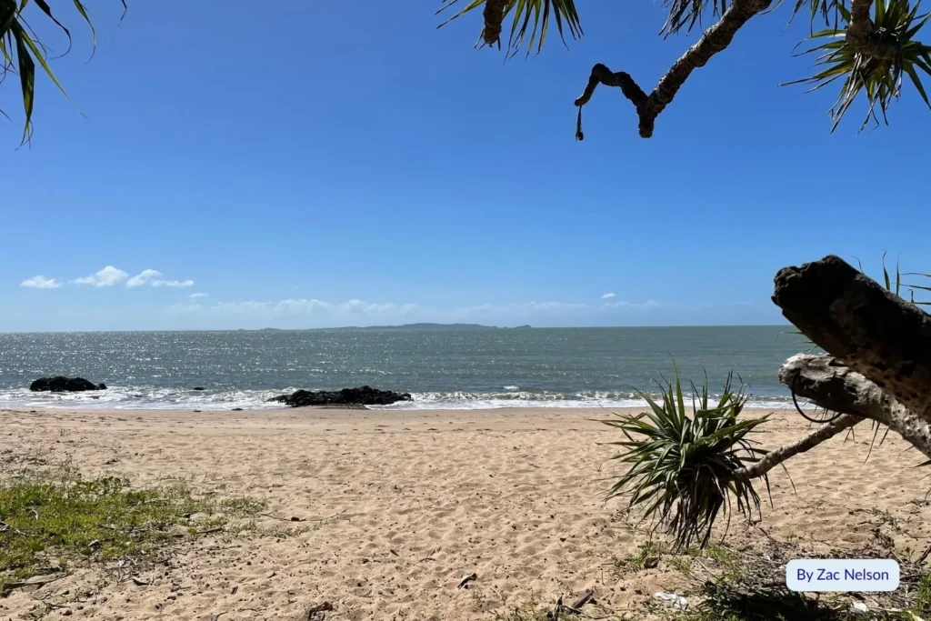 Cooee Bay Beach on the Capricorn Coast, Queensland, with pandanus trees framing the sandy shoreline and calm blue ocean