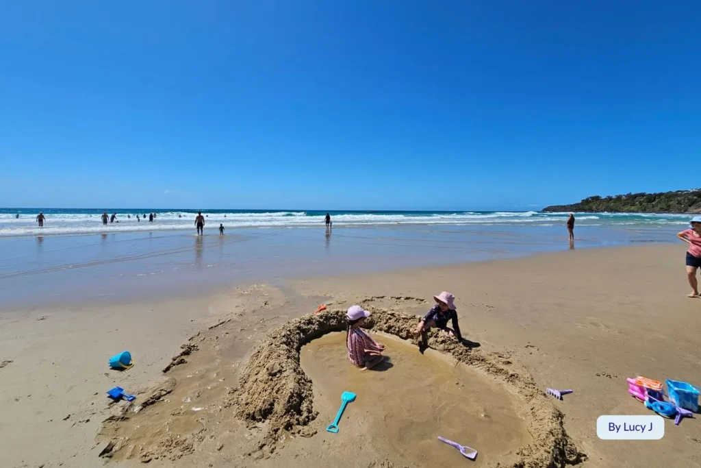Children building sandcastles and families paddling in the shallow waves at Coolum Beach, a family-friendly Sunshine Coast destination with soft sand and gentle surf.