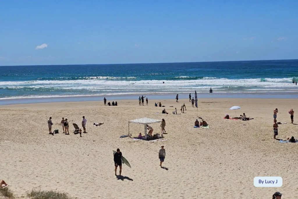 Beachgoers enjoying the sun and surf at Coolum Beach, Sunshine Coast, Queensland, with swimmers and surfers along the patrolled shoreline.