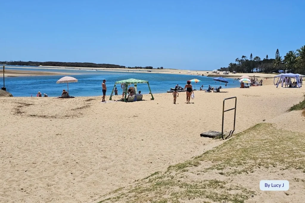 Families relaxing on the golden sands of Cotton Tree Beach, Sunshine Coast, Queensland, beside the calm Maroochy River estuary under clear blue skies.