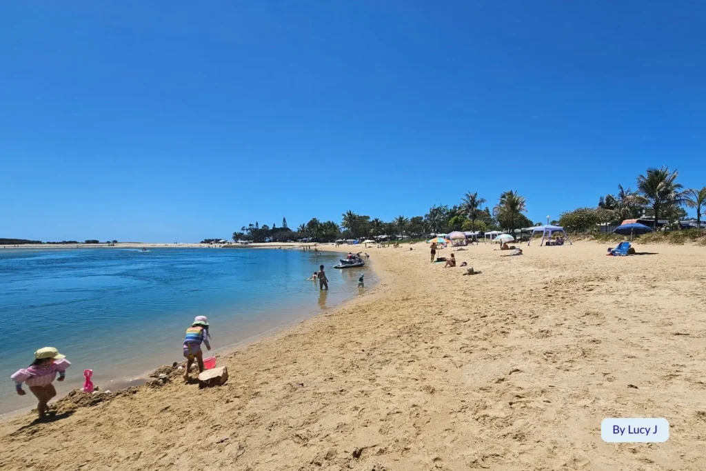 Children playing on the shoreline and people swimming in the gentle waters of Cotton Tree Beach, a peaceful estuary beach in Maroochydore, Sunshine Coast.