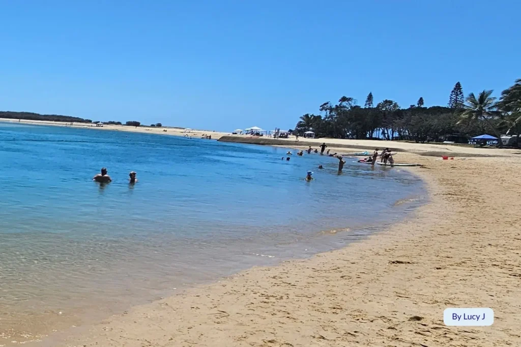 Swimmers enjoying the tranquil blue water and soft sandy shoreline at Cotton Tree Beach, Sunshine Coast, Queensland, near Maroochy River inlet.