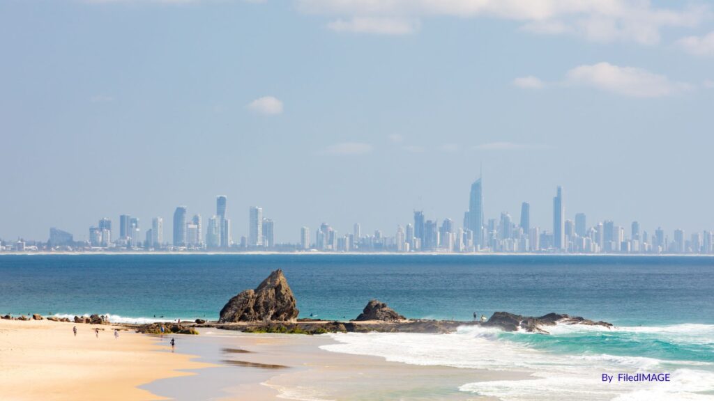 View of Currumbin Alley with surfers near the rocky headland and Surfers Paradise skyline in the distance, Gold Coast, Queensland.