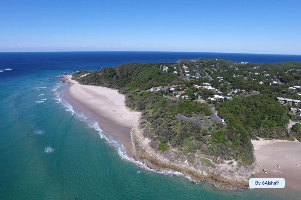 Aerial view of Cylinder Beach, North Stradbroke Island, showing its curved shoreline and lush green headland
