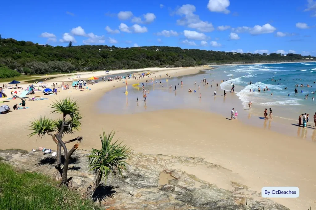 Busy summer day at Cylinder Beach, North Stradbroke Island, with swimmers and families enjoying the golden sand and turquoise waves.