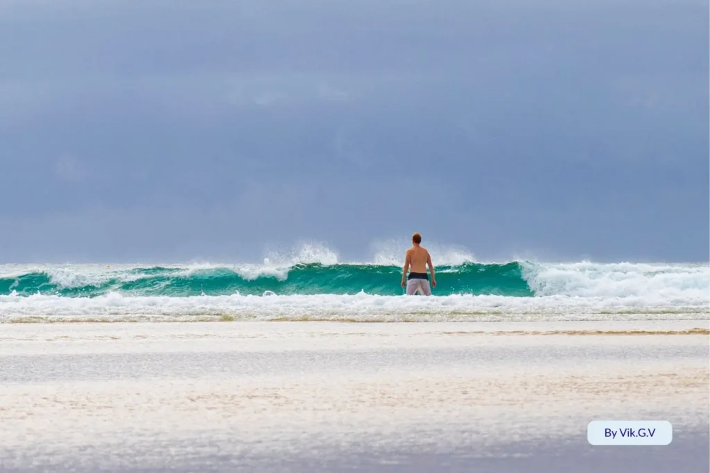 Surfer watching waves at Cylinder Beach on North Stradbroke Island under cloudy skies and soft rolling surf.