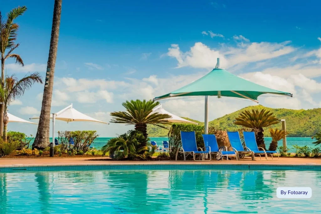Resort pool with sun loungers and umbrellas overlooking turquoise water and palm trees on Daydream Island, Whitsundays, Queensland.