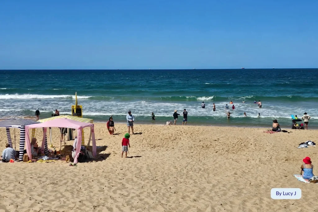Families enjoying the surf at Dicky Beach, Caloundra, Sunshine Coast, Queensland, with sun shelters on the golden sand and swimmers between lifeguard flags.