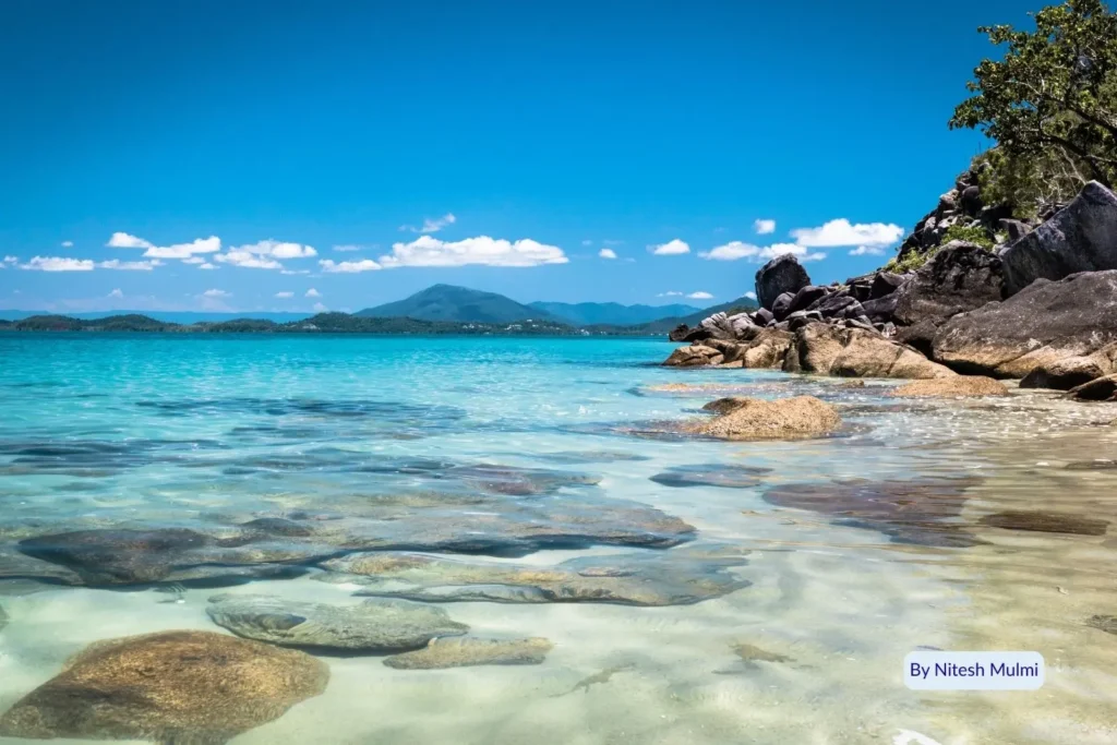 Crystal-clear turquoise water and granite rocks along the shoreline of Dunk Island with rainforest hills in the background, Cassowary Coast, Queensland, Australia