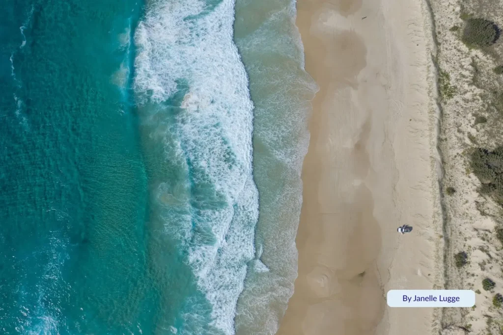 Drone shot of Moreton Island’s ocean side with foamy waves breaking onto the beach, showing pristine dunes and deep blue Pacific waters.