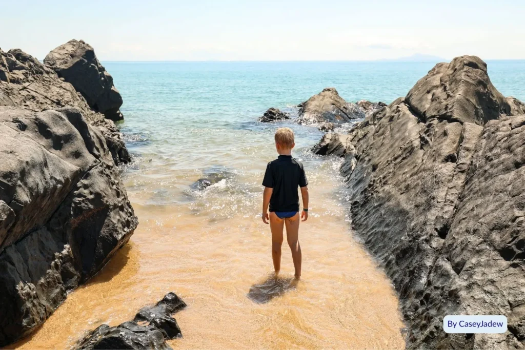 Visitor exploring the rocky shoreline at Eimeo Beach near Mackay, Queensland, where golden sand meets clear blue ocean and coastal cliffs.