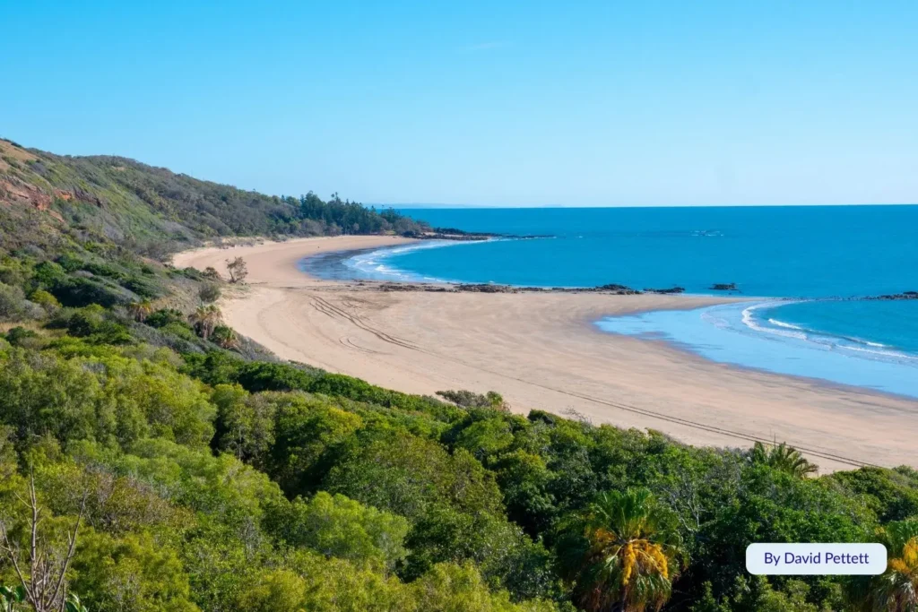 Aerial view of Emu Park Beach, Queensland, with golden sand curving around the bay, lush green hills, and clear blue ocean