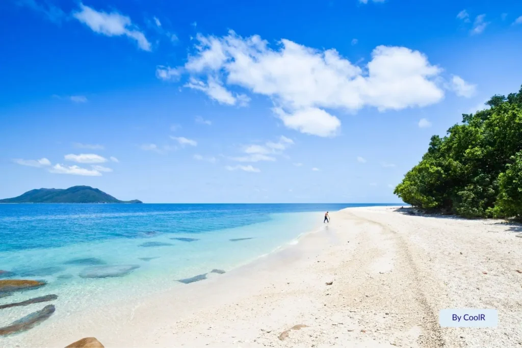White coral sand and turquoise water at Fitzroy Island with lush rainforest and mountains in the distance, Cairns Region, Queensland, Australia