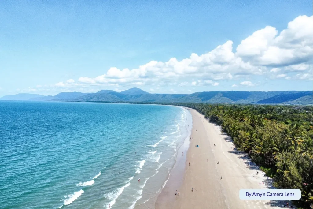 Aerial view of Four Mile Beach with calm blue ocean, lush tropical coastline, and mountain views near Port Douglas, Queensland, Australia