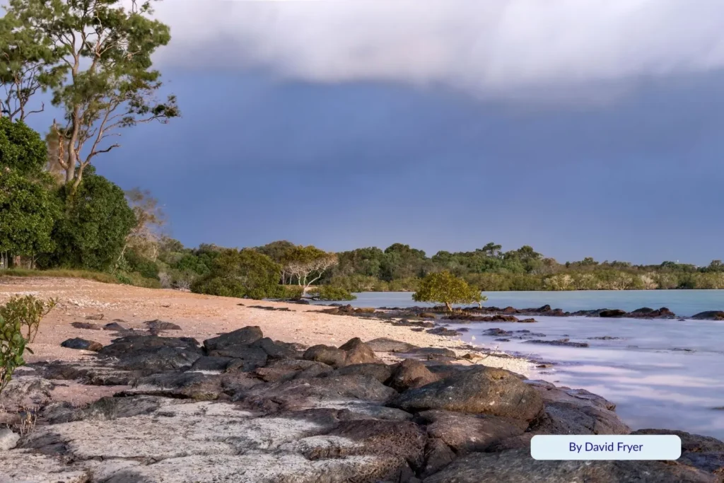 Rocky shoreline and calm blue water at Gatakers Bay Point Vernon, framed by native trees and coastal vegetation in Hervey Bay Queensland.