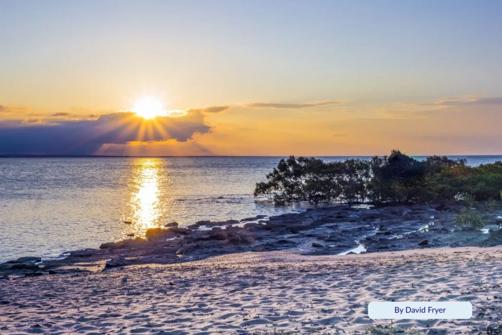 Sunset over Gatakers Bay Beach at Point Vernon, Hervey Bay, with golden light reflecting on calm waters and rocky shoreline framed by mangroves.
