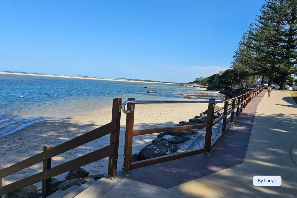 Scenic walkway along the waterfront with pine trees and clear shallow water at Golden Beach, Caloundra, Sunshine Coast, Queensland.