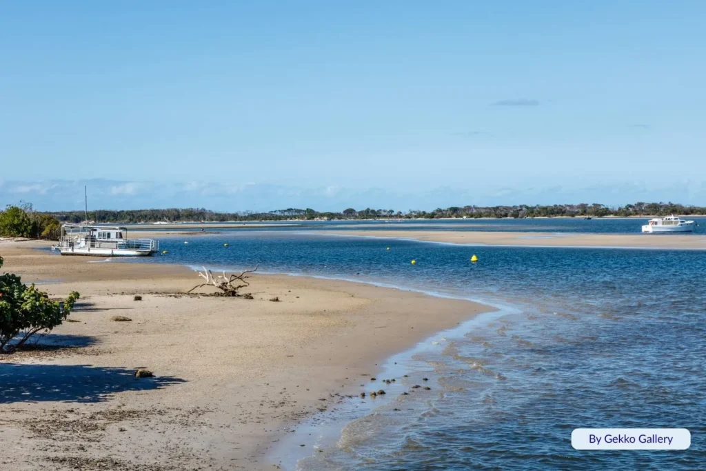 Low tide at Golden Beach, Sunshine Coast, showing calm estuary waters, exposed sandy shoreline, and a houseboat anchored near the edge of Pumicestone Passage.