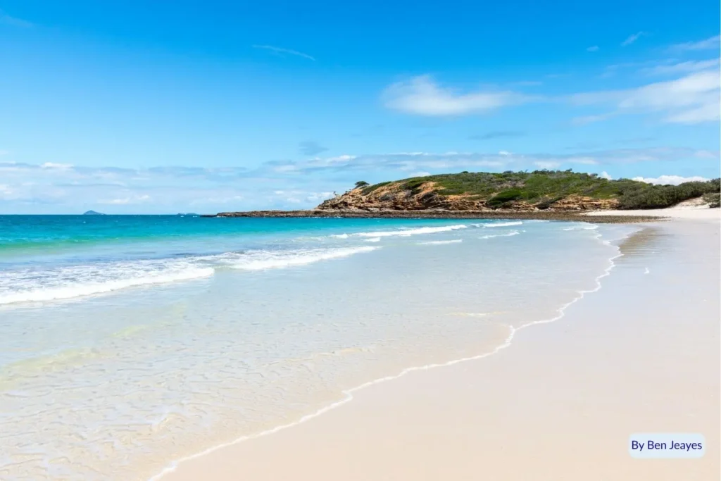 Wide sandy beach with gentle waves and rocky headland at Great Keppel Island, Capricorn Coast, Queensland, under bright blue skies