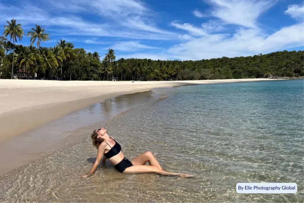 Woman relaxing in the shallow clear water at Great Keppel Island, Queensland, surrounded by palm trees and tropical scenery
