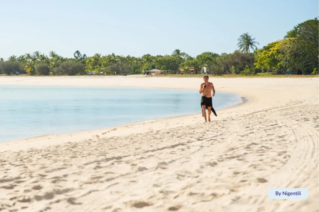 Man walking along the soft white sand at Great Keppel Island, Queensland, with calm turquoise water and palm-fringed shoreline