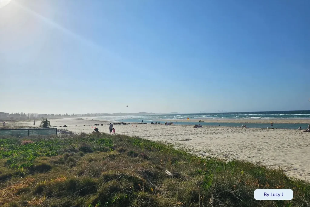 Wide sandy shoreline of Greenmount Beach with people sunbathing and swimming under bright sunshine, Coolangatta, Gold Coast, Queensland.