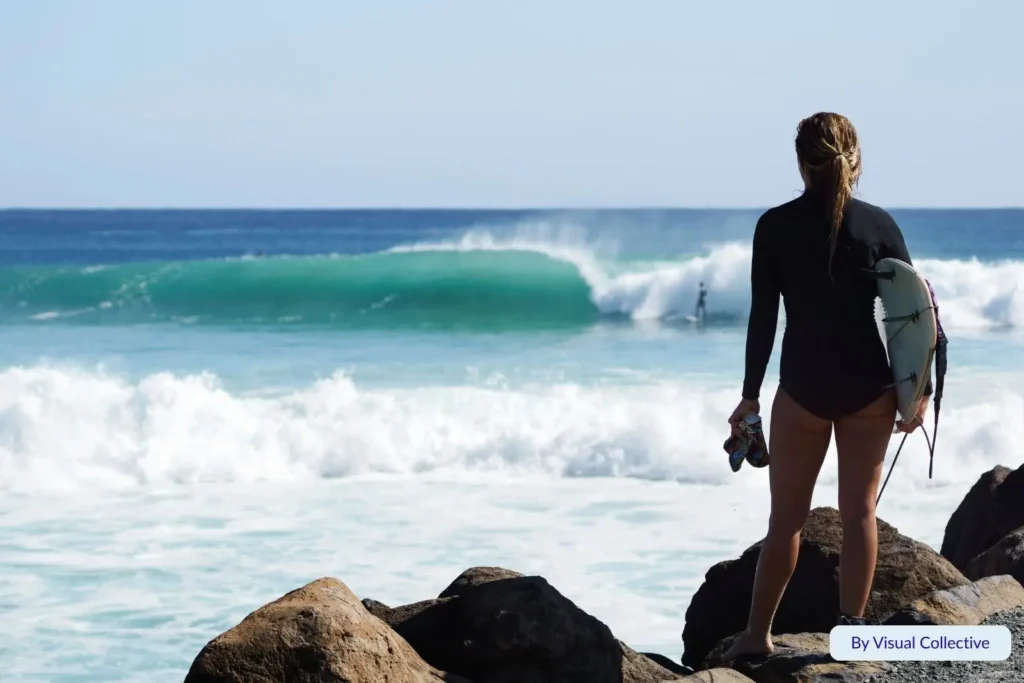Female surfer standing on rocks watching waves at Greenmount Beach, Coolangatta, Gold Coast, Queensland, a popular surf spot on the southern coast.