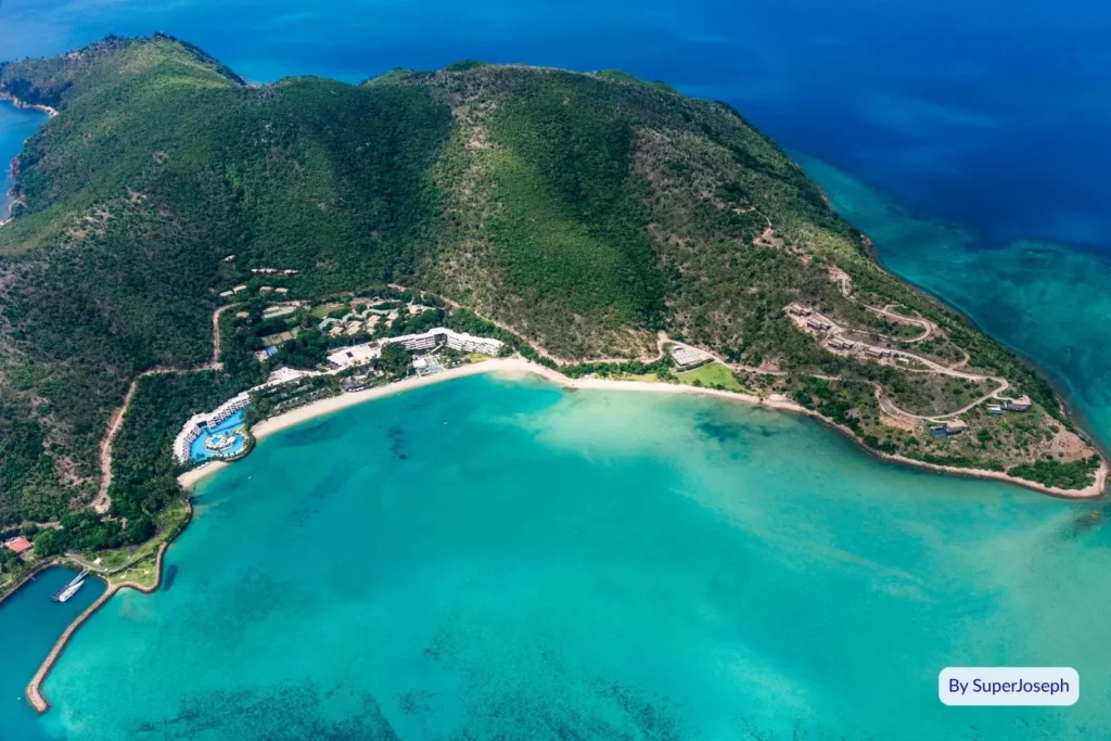 Aerial view of Hamilton Island showing lush green hills, turquoise water, and resort area surrounded by the Great Barrier Reef, Whitsundays, Queensland.
