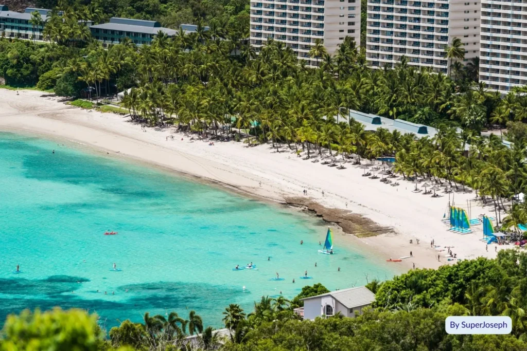 Catseye Beach on Hamilton Island with people swimming and paddleboarding in clear blue water beside palm-lined resort buildings, Whitsundays, Queensland.
