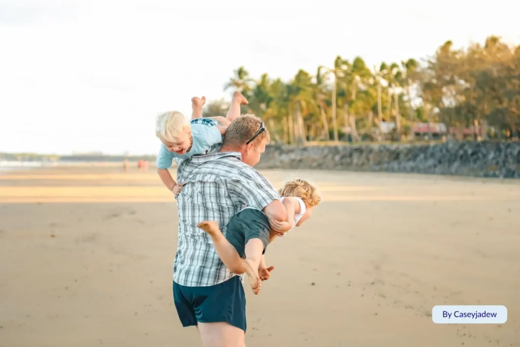 Family playing on the golden sand at Harbour Beach in Mackay, Queensland, with palm trees and sunset light in the background