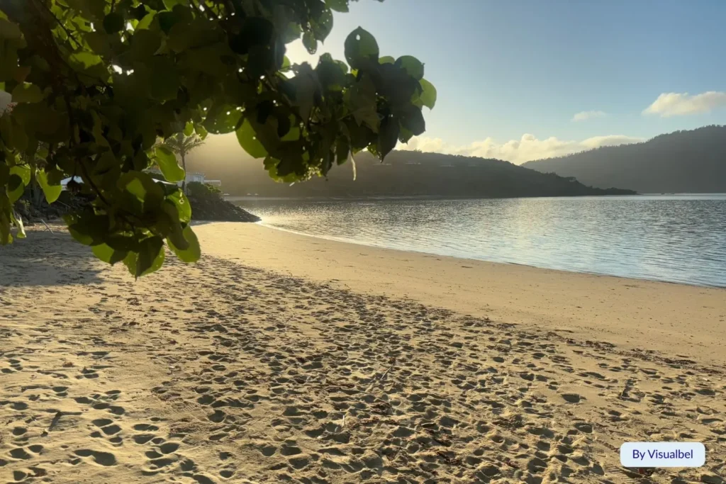 Golden sunrise over a calm sandy beach on Hayman Island with gentle waves and mountain silhouettes, Whitsundays, Queensland.