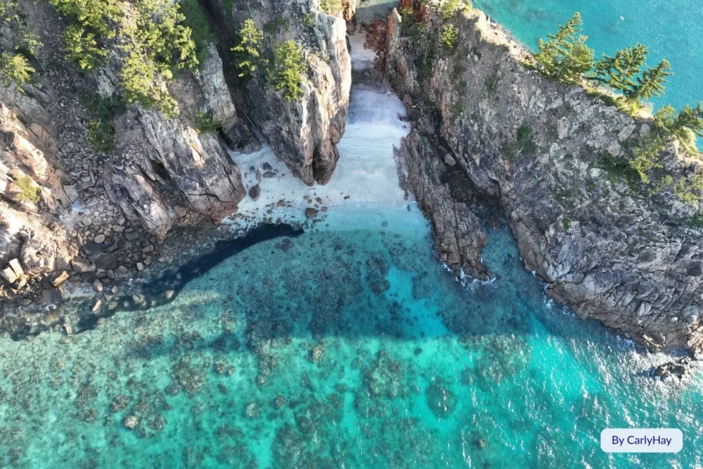 Aerial view of Blue Pearl Bay’s dramatic cliffs and turquoise lagoon on Hayman Island, surrounded by coral reef and clear Coral Sea waters, Queensland.