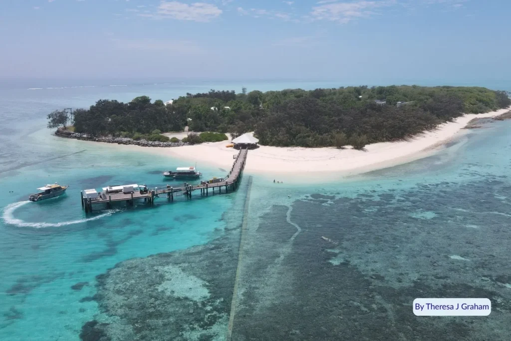 Aerial view of Heron Island surrounded by turquoise reef waters, showing jetty, boats, and coral lagoon in the southern Great Barrier Reef, Queensland.