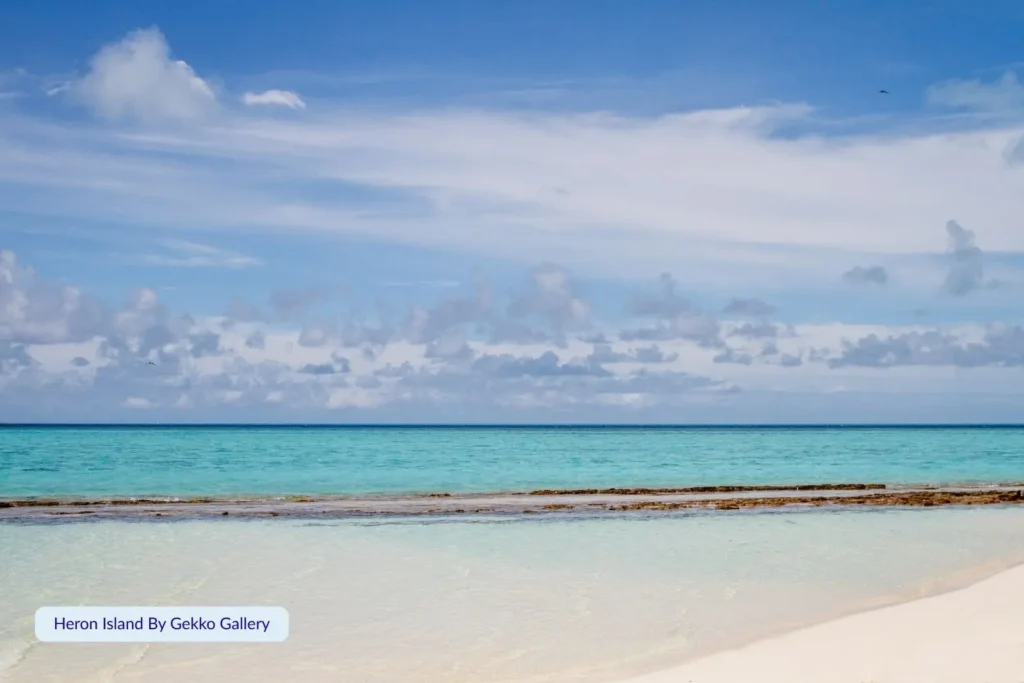White sandy shoreline and turquoise lagoon at Heron Island on the Great Barrier Reef, with calm clear waters and soft clouds above, Gladstone Region, Queensland.