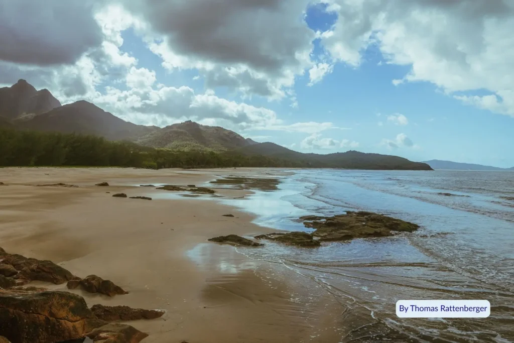 Wide sandy beach and dramatic mountains under cloudy sky at Hinchinbrook Island, Far North Queensland.