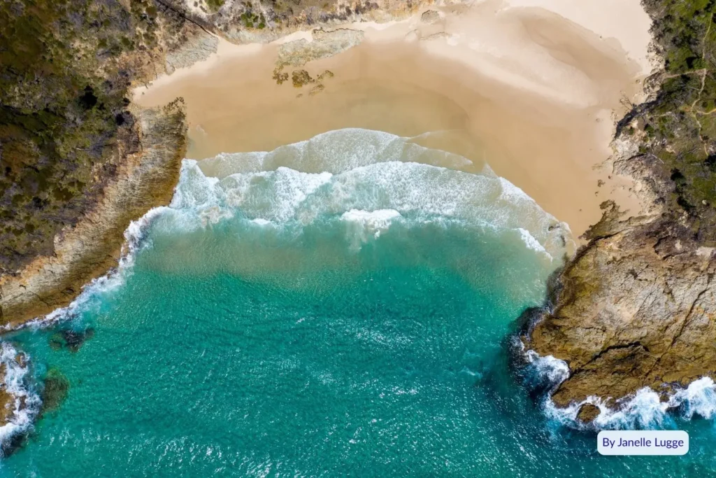 Aerial view of Honeymoon Bay Moreton Island featuring crystal-clear water, rocky cliffs, and an untouched sandy shoreline surrounded by coastal bushland.