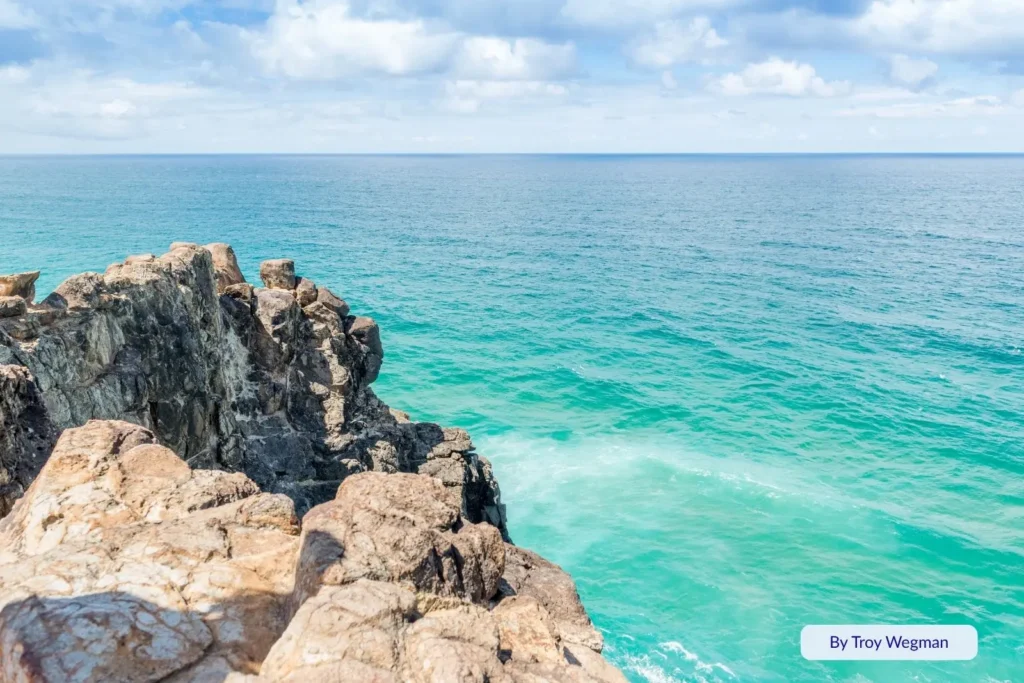 Panoramic view from Indian Head lookout showing turquoise waves crashing against rugged volcanic cliffs on Fraser Island’s eastern coast.