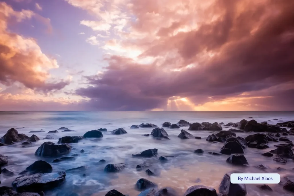 Rocky shoreline at Kellys Beach, Bundaberg, Queensland, during a dramatic sunset with purple and orange clouds reflecting over the ocean.