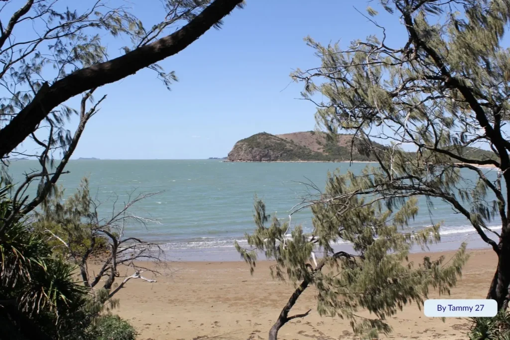 View of Kemp Beach near Yeppoon, Queensland, with trees framing the sandy shore and Bluff Point rising in the background under a clear blue sky.