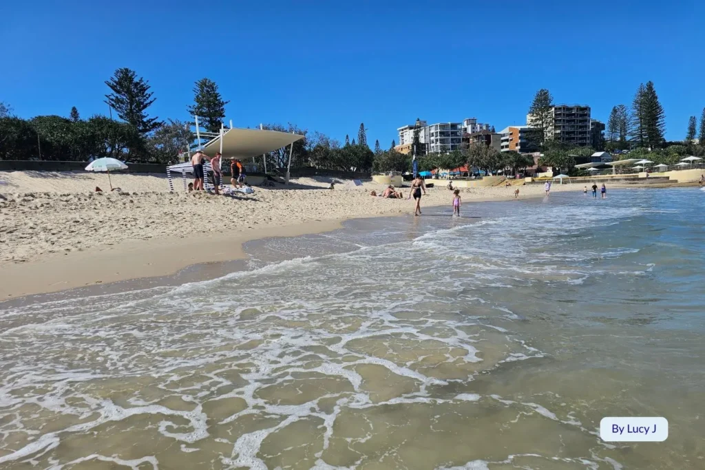 Families enjoying the surf and sunshine at Kings Beach, Caloundra, with golden sand, gentle waves, and beachfront apartments along the Sunshine Coast, Queensland